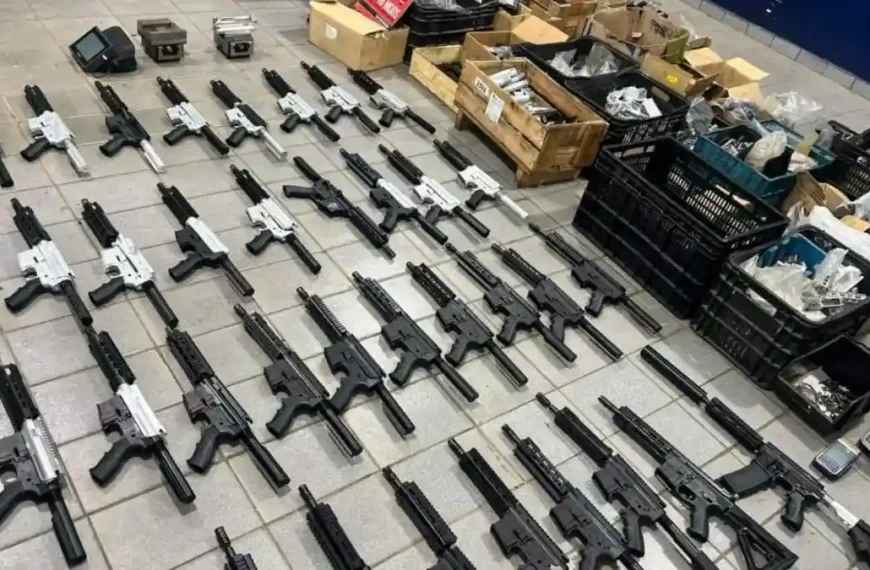 A imagem mostra dezenas de fuzis enfileirados no chão, em diferentes estágios de montagem, com cores preta e prateada. Ao fundo, há caixas e caixotes cheios de peças, evidenciando um arsenal clandestino desmontado em operação policial.