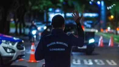 CGM: da vigilância à Polícia Municipal-A imagem mostra um agente da Guarda Municipal de Londrina de costas, usando uniforme azul escuro, com o braço levantado em um gesto de sinalização.