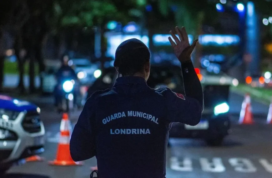 CGM: da vigilância à Polícia Municipal-A imagem mostra um agente da Guarda Municipal de Londrina de costas, usando uniforme azul escuro, com o braço levantado em um gesto de sinalização.