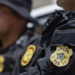 Alagoas: vítima de estelionato. A imagem mostra dois agentes da Polícia Civil em uniforme preto. O foco está no brasão bordado no braço do colete tático, com a inscrição "Polícia Civil".