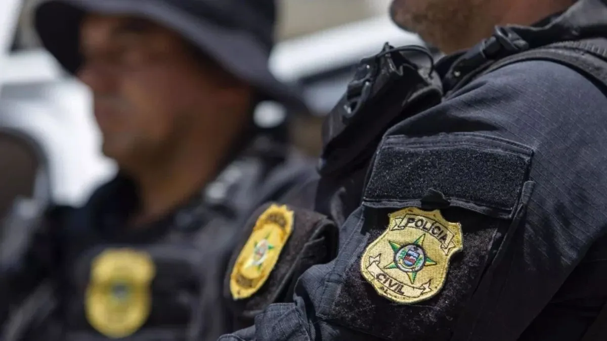 Alagoas: vítima de estelionato. A imagem mostra dois agentes da Polícia Civil em uniforme preto. O foco está no brasão bordado no braço do colete tático, com a inscrição "Polícia Civil".