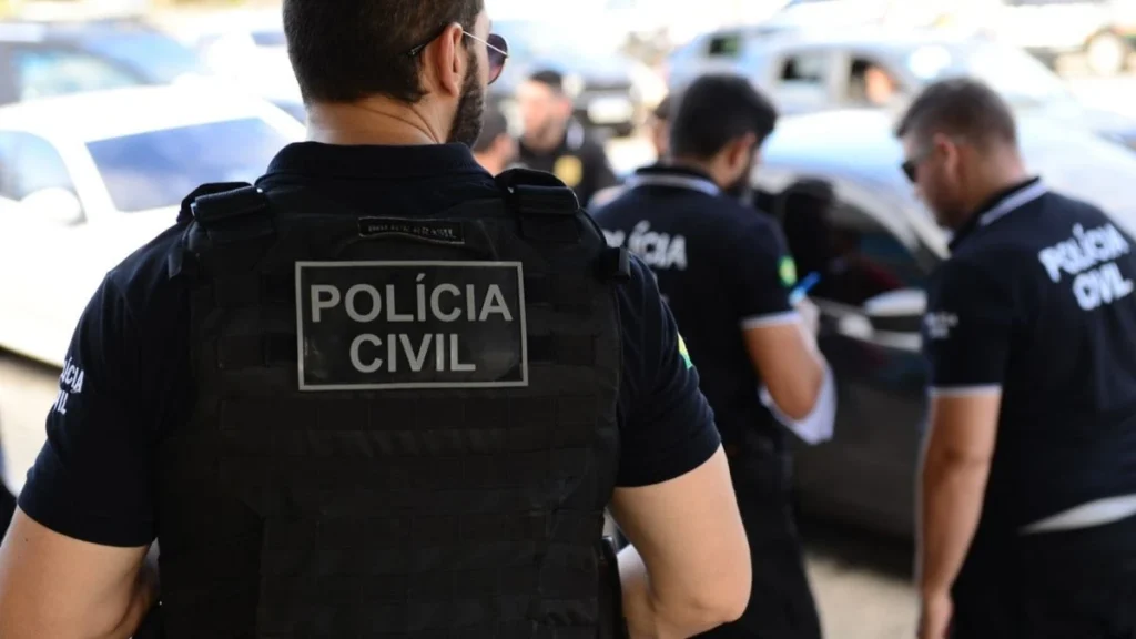 A imagem mostra agentes da Polícia Civil em operação, usando coletes táticos com a identificação da corporação. Alguns policiais estão próximos a veículos, conversando e anotando informações.
