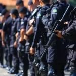 Ciclo completo: o debate que o Brasil finge não existir-A imagem mostra uma fileira de policiais fardados alinhados, vestindo uniformes escuros e portando armas, em formação durante um evento ou cerimônia ao ar livre.