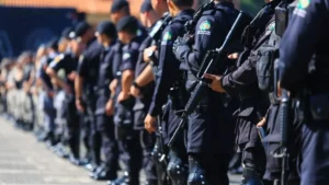 Ciclo completo: o debate que o Brasil finge não existir-A imagem mostra uma fileira de policiais fardados alinhados, vestindo uniformes escuros e portando armas, em formação durante um evento ou cerimônia ao ar livre.
