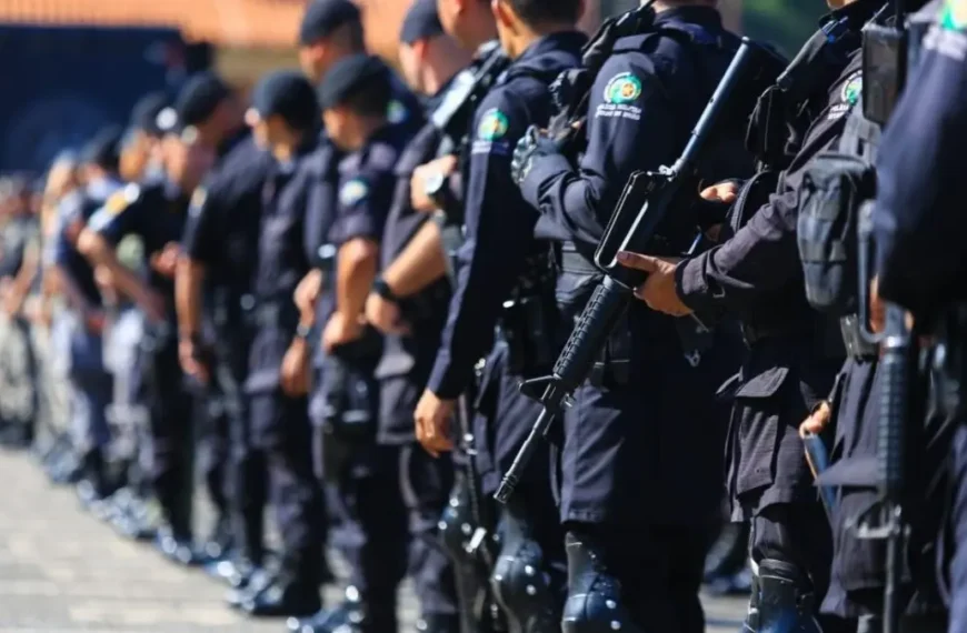 Ciclo completo: o debate que o Brasil finge não existir-A imagem mostra uma fileira de policiais fardados alinhados, vestindo uniformes escuros e portando armas, em formação durante um evento ou cerimônia ao ar livre.