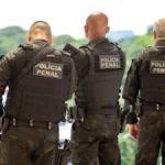 Agentes da Polícia Penal em uniforme tático, de costas, durante operação externa de segurança