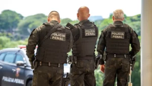 Agentes da Polícia Penal em uniforme tático, de costas, durante operação externa de segurança