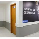 Corredor interno de uma Central de Flagrantes em Alagoas, com portas de atendimento e painel na parede indicando a área de registro de boletim de ocorrência (falsas comunicações de crimes)