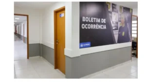 Corredor interno de uma Central de Flagrantes em Alagoas, com portas de atendimento e painel na parede indicando a área de registro de boletim de ocorrência (falsas comunicações de crimes)