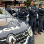 Guardas civis municipais uniformizados estão alinhados ao lado de viaturas da GCM de Ribeirão Pires durante uma formação operacional em via pública.