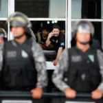 Polícia Penal. Aposentadoria policial especial. Agentes penitenciários dentro do Ministério da Justiça durante protesto em Brasília, enquanto policiais fazem a contenção na área externa do prédio.