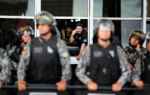 Polícia Penal. Aposentadoria policial especial. Agentes penitenciários dentro do Ministério da Justiça durante protesto em Brasília, enquanto policiais fazem a contenção na área externa do prédio.